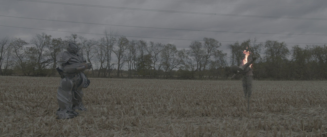An armored character faces a burning scarecrow figure in a harvested field.